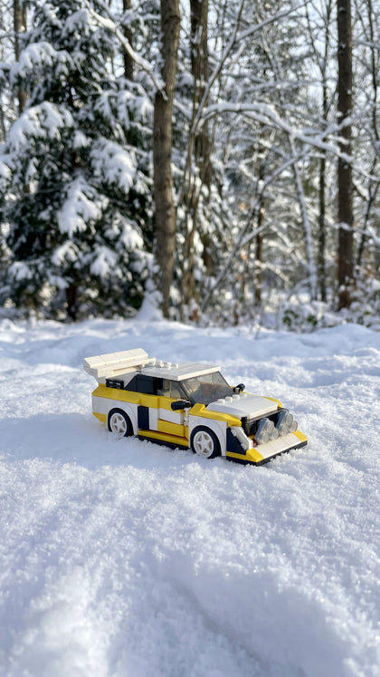 A white and yellow brick-built rally car standing in fresh snow