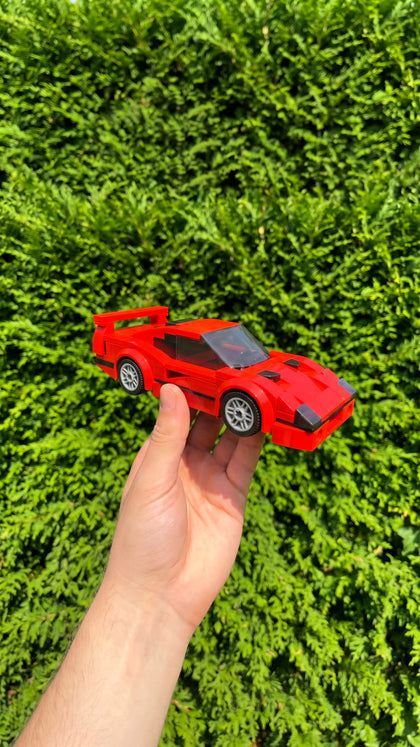 A red brick-built supercar held up in front of a green hedge