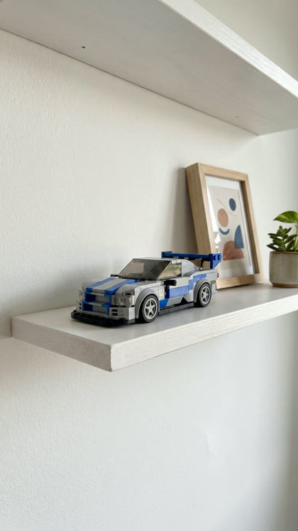 A silver and blue brick-built sports car on a white shelf next to a framed print