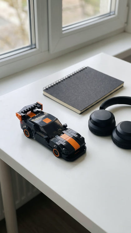 A black and orange brick-built sports car on a white desk next to headphones