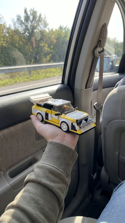 A white and yellow brick-built rally car held up inside a car