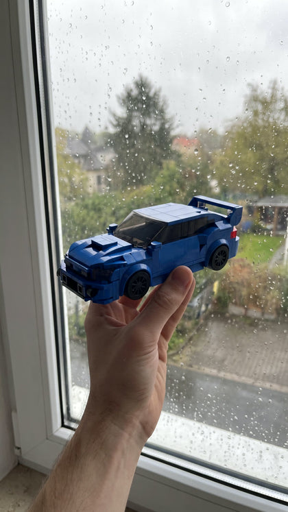 A blue brick-built rally saloon held up by a rainy window
