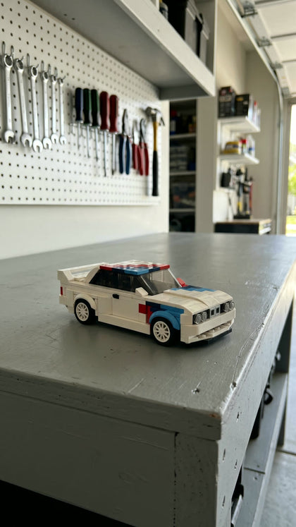 A white brick-built touring car with racing stripes on a tidy garage workbench