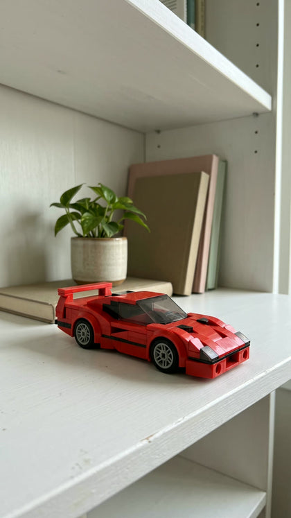 A red brick-built supercar on a white bookshelf next to a plant