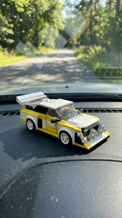 A white and yellow brick-built rally car on the dashboard of a car