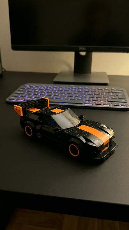 A black and orange brick-built sports car on a black desk in front of a keyboard